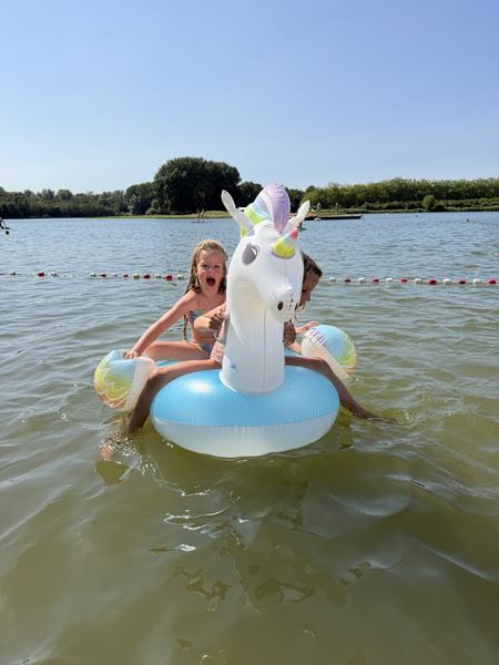 Two girls are floating on a unicorn-shaped inflatable in a lake on a sunny day